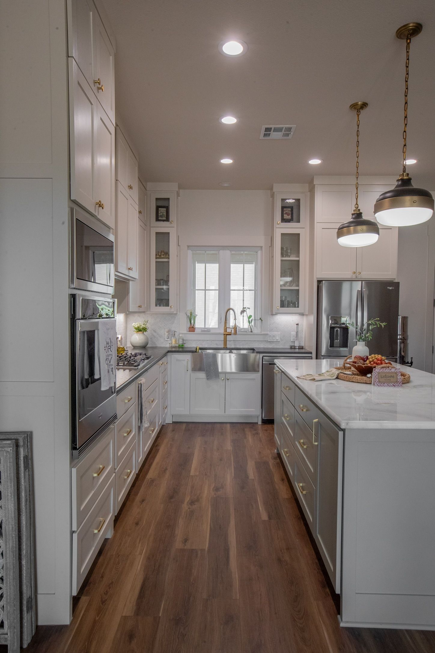White kitchen with dark wood floors and island, stainless steel appliances, pendant lights.