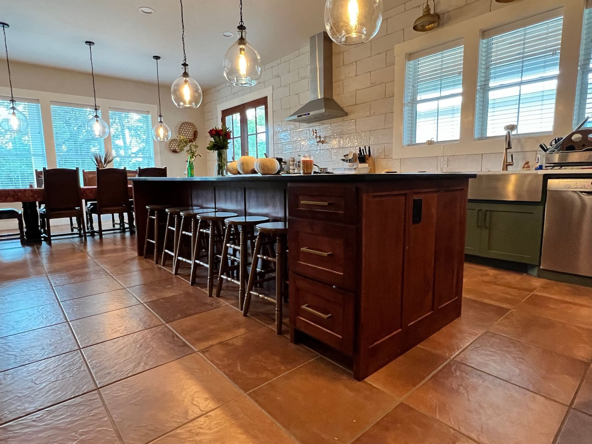 Kitchen with dark wood island, stools, and pendant lights. Brown tiled floor, and stainless steel appliances.