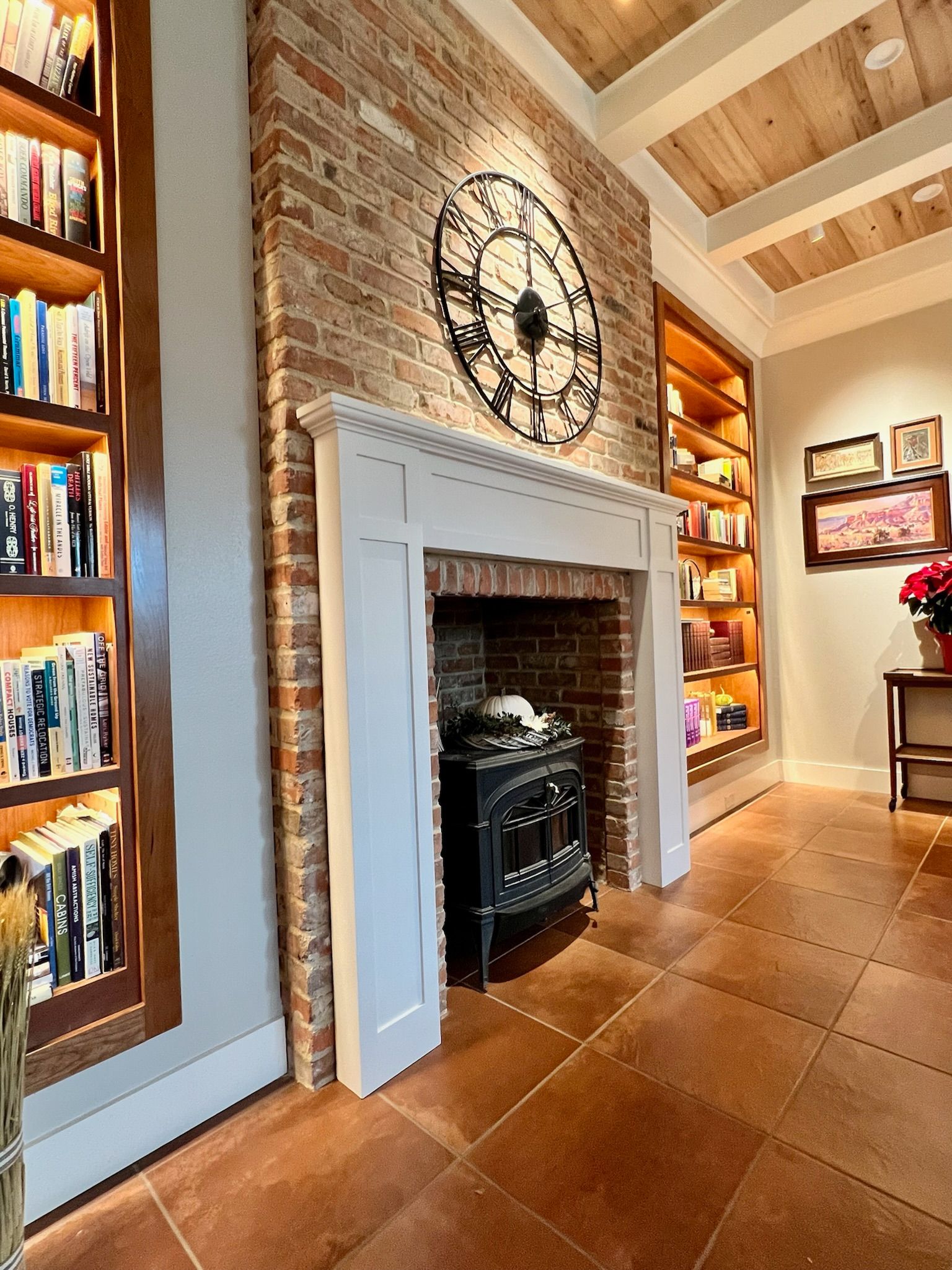 Fireplace with brick wall, bookshelves, ornate clock, and tile floor in a room.