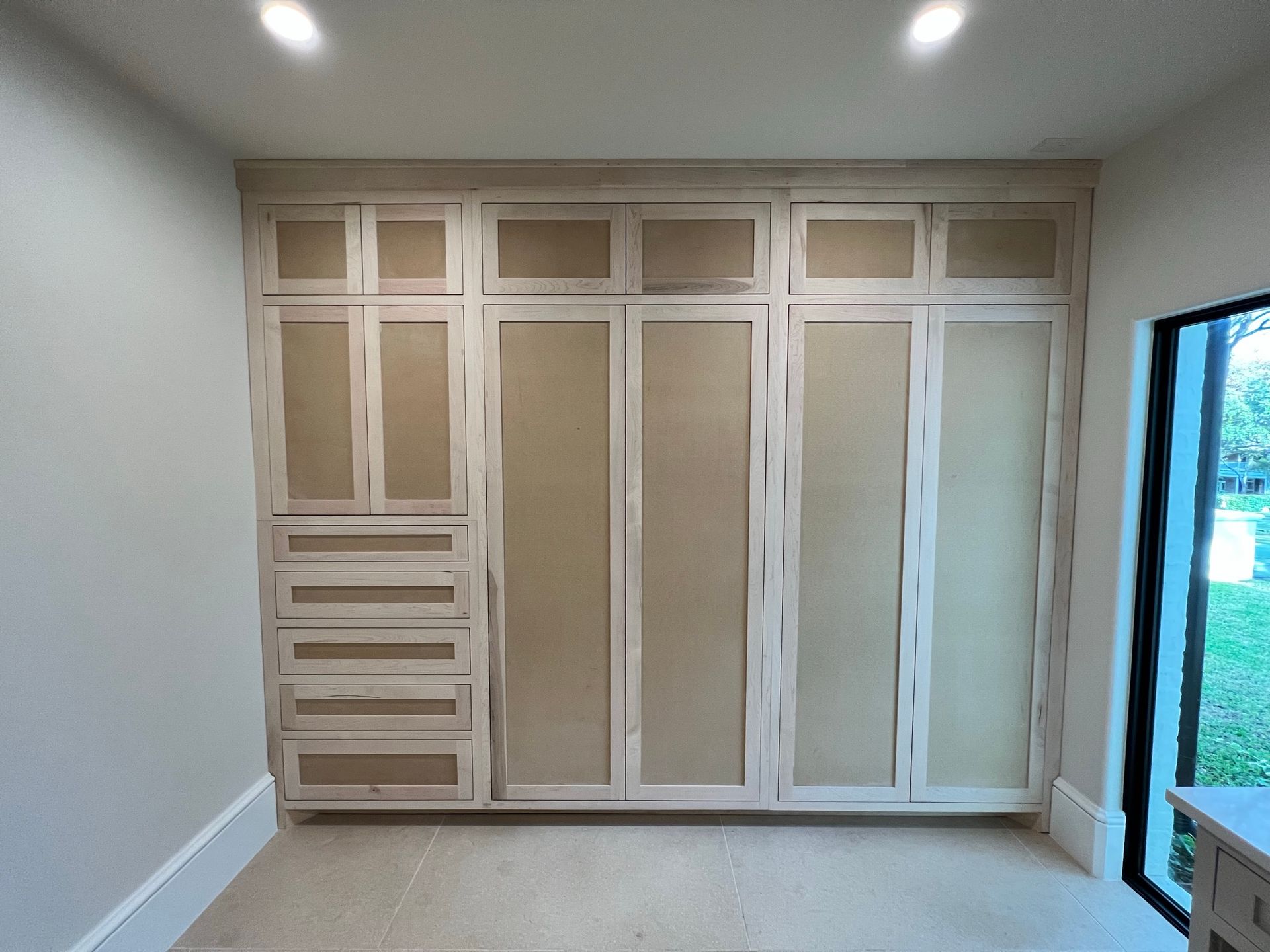Built-in light wood closet unit with doors and drawers in a room with a window.