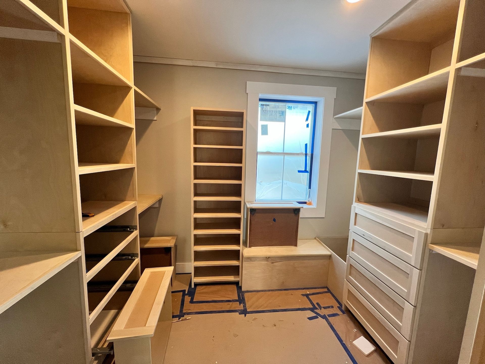 Walk-in closet under construction with light wood shelving, drawers, and a window.
