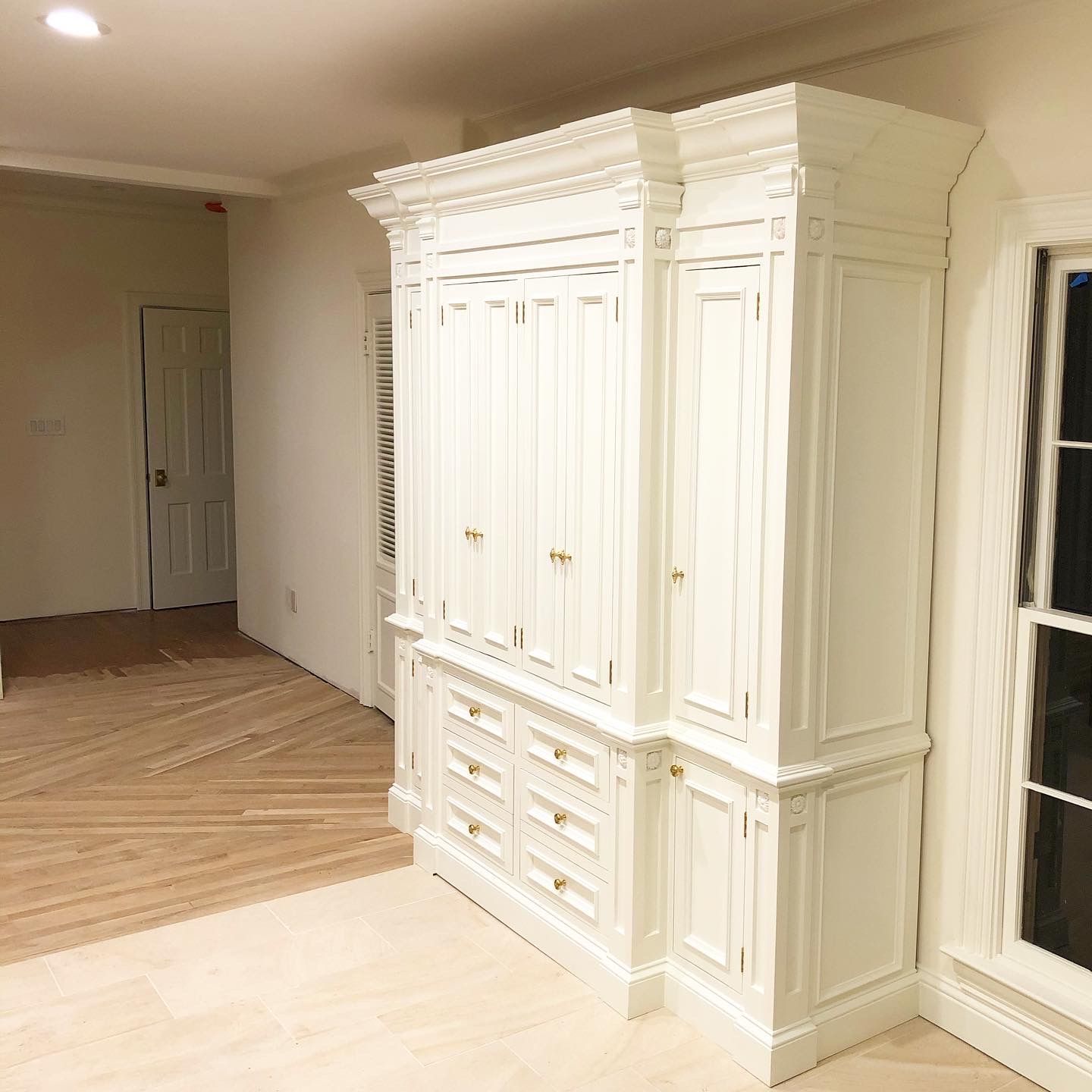 White built-in cabinetry with drawers and doors in a room with hardwood floors and a window.
