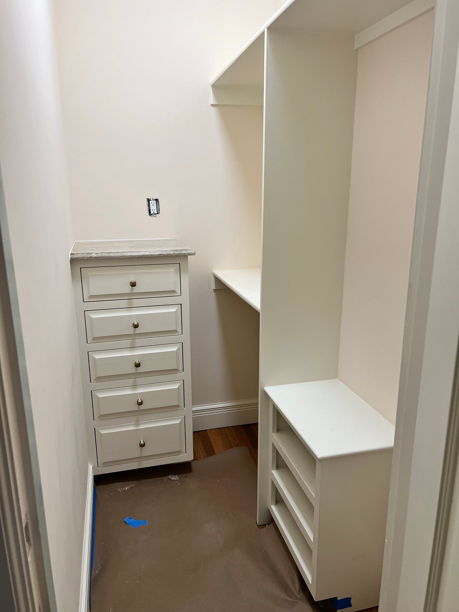 Small walk-in closet with white shelves and drawers, wooden floor, and light pink walls.