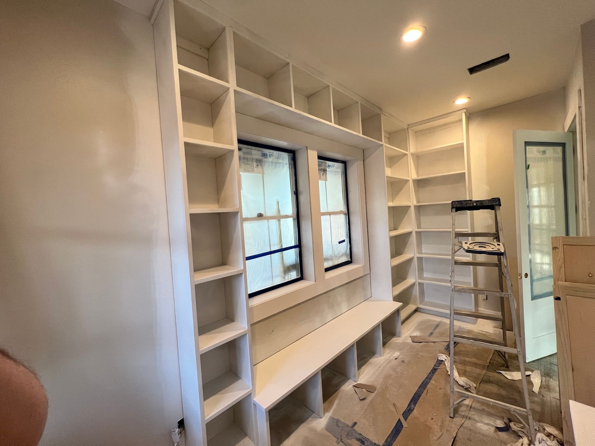 Built-in white bookshelves surround a window with a bench. A ladder stands nearby.