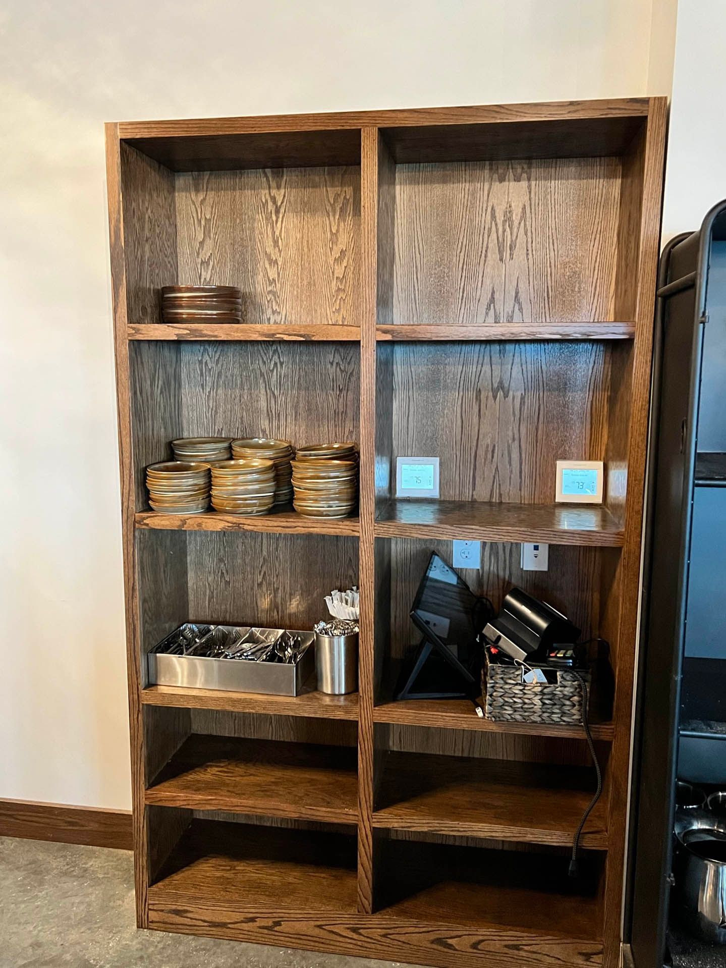 Wooden bookshelf filled with various items; plates, containers, and electronics.