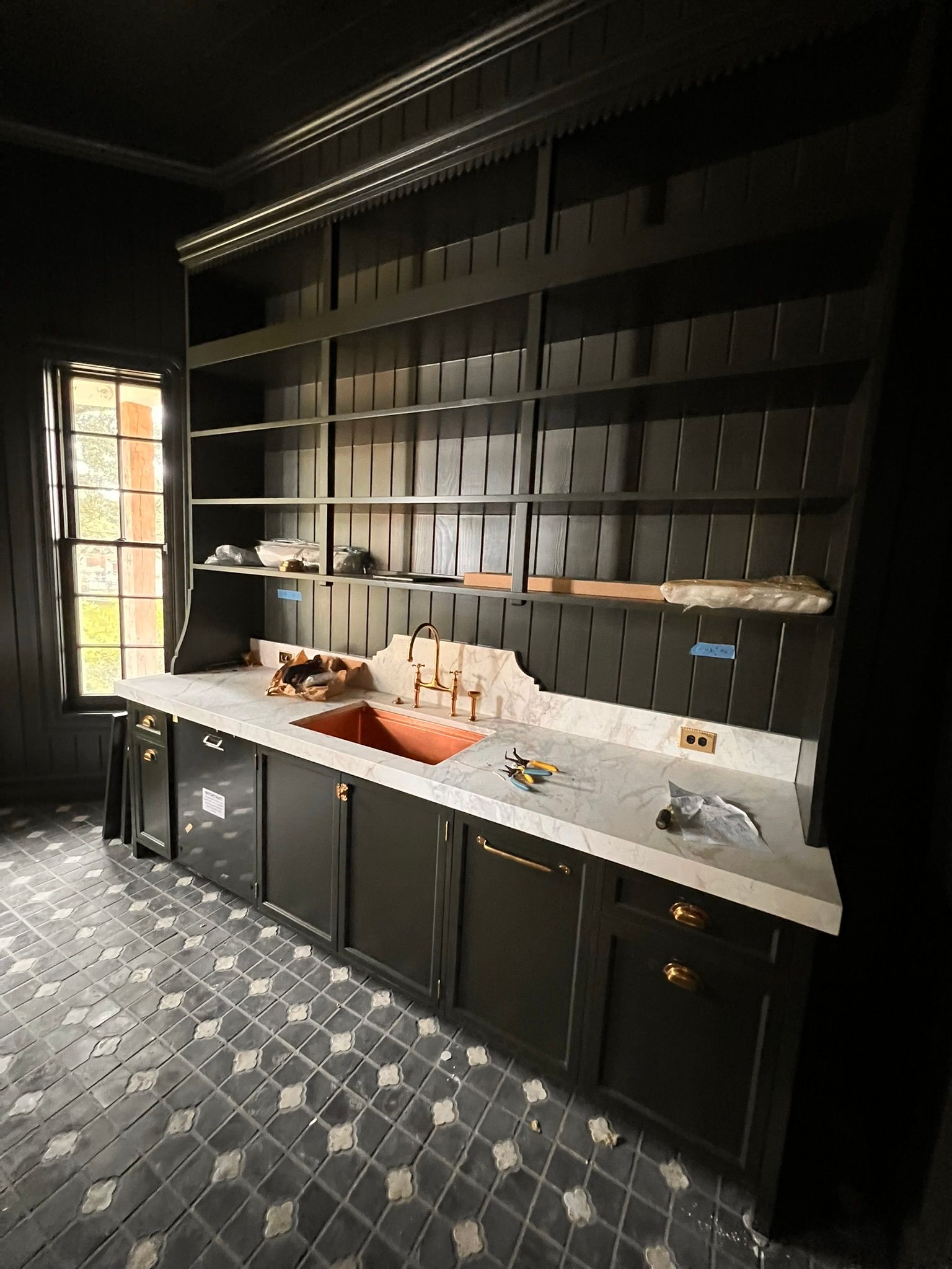 Black built-in shelves and cabinets with a sink. Light counter, copper sink, and patterned floor.