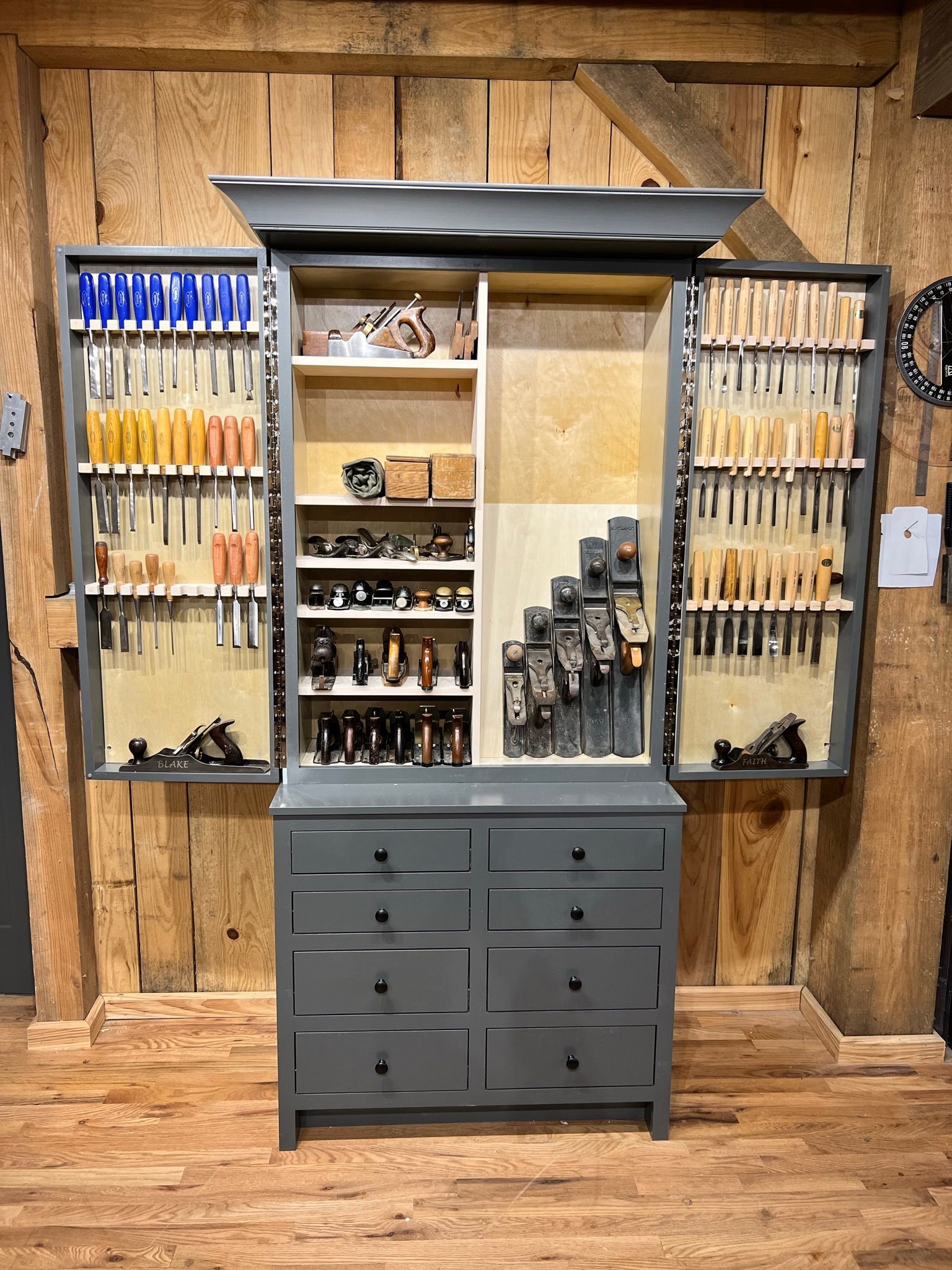 Gray tool cabinet with drawers and open doors revealing organized hand tools against a wood background.