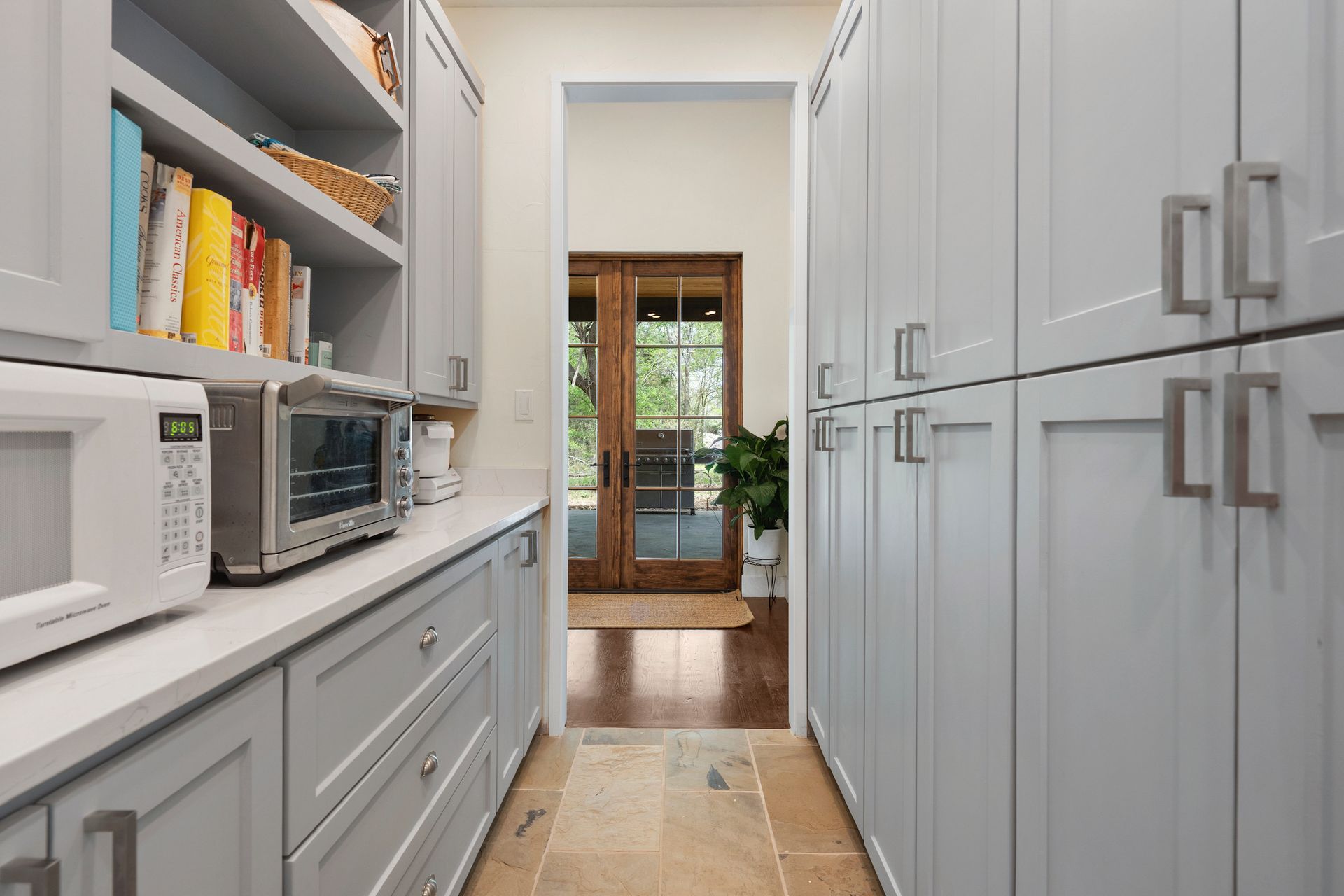 Long, narrow pantry with gray cabinets, microwave, and doorway.