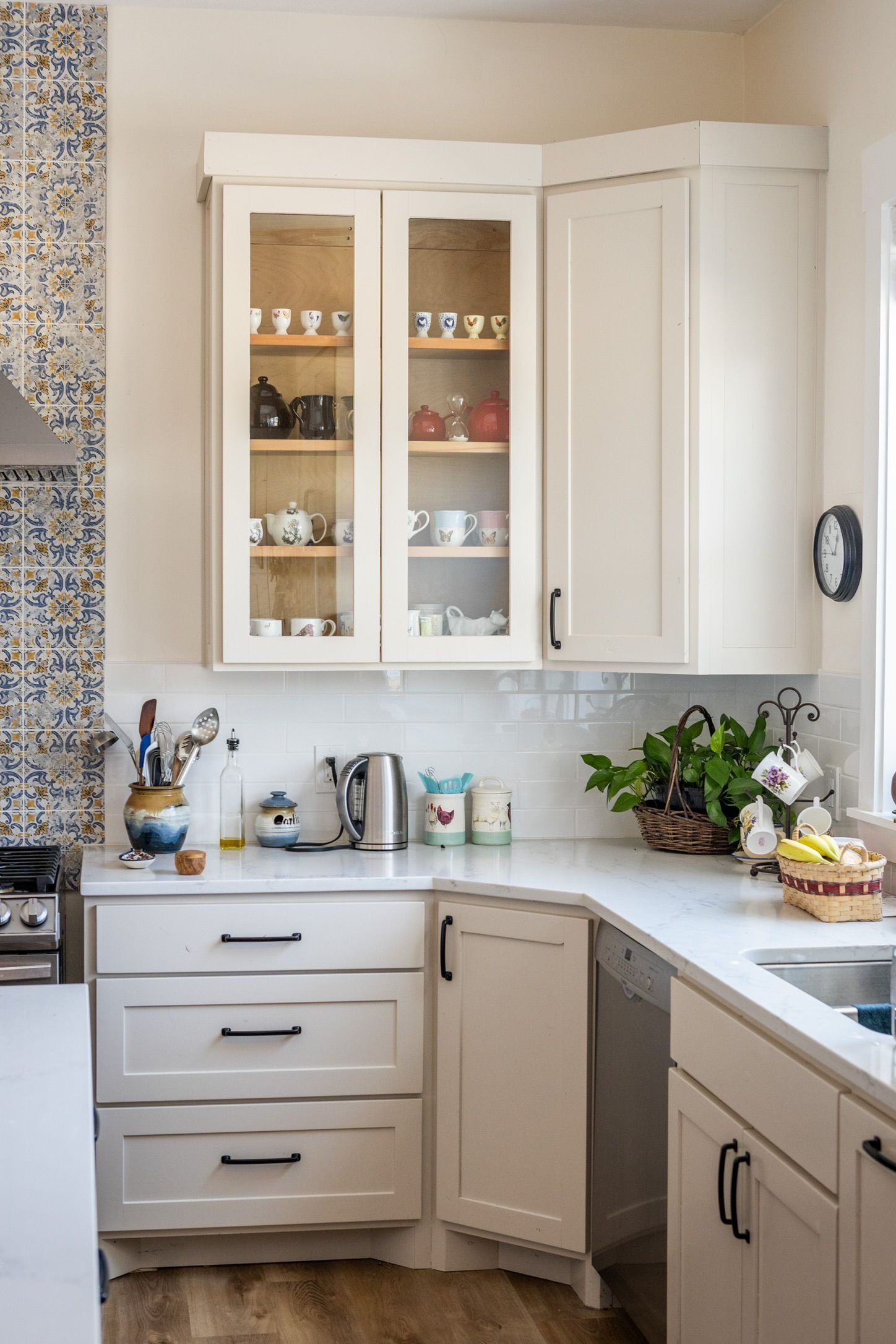 White kitchen cabinets with glass-front display cabinet, white countertops, and blue and white tile backsplash.