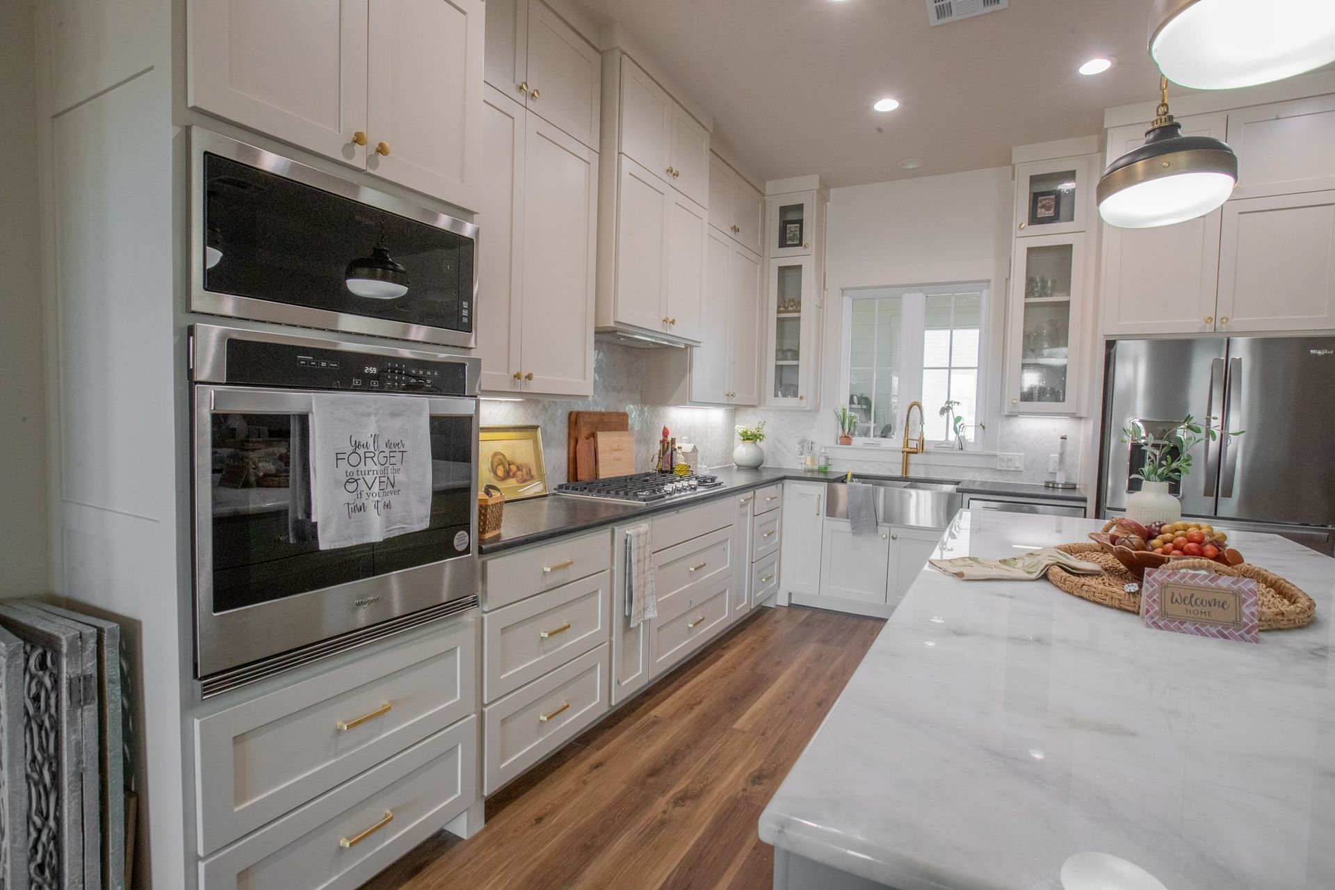 Bright white kitchen with stainless steel appliances, marble island, and wooden floors.