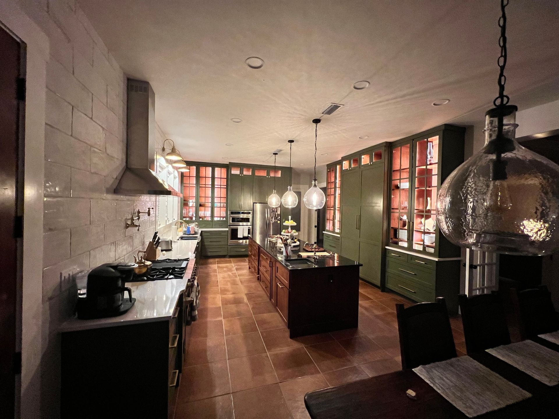 Spacious kitchen with a red island, green cabinets, and hanging lights.