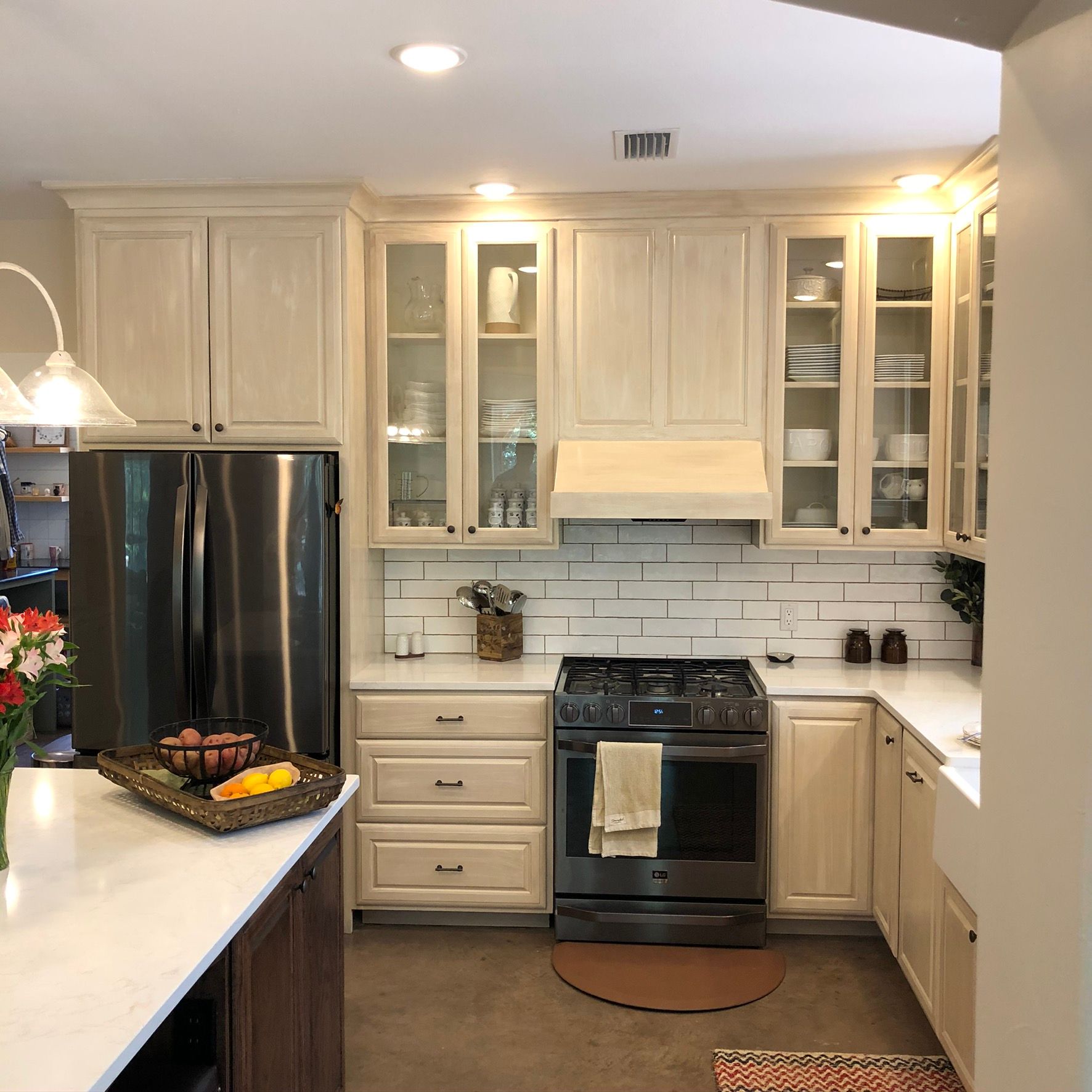 Cream-colored kitchen with stainless steel appliances, subway tile backsplash, and dark wooden island with white countertop.