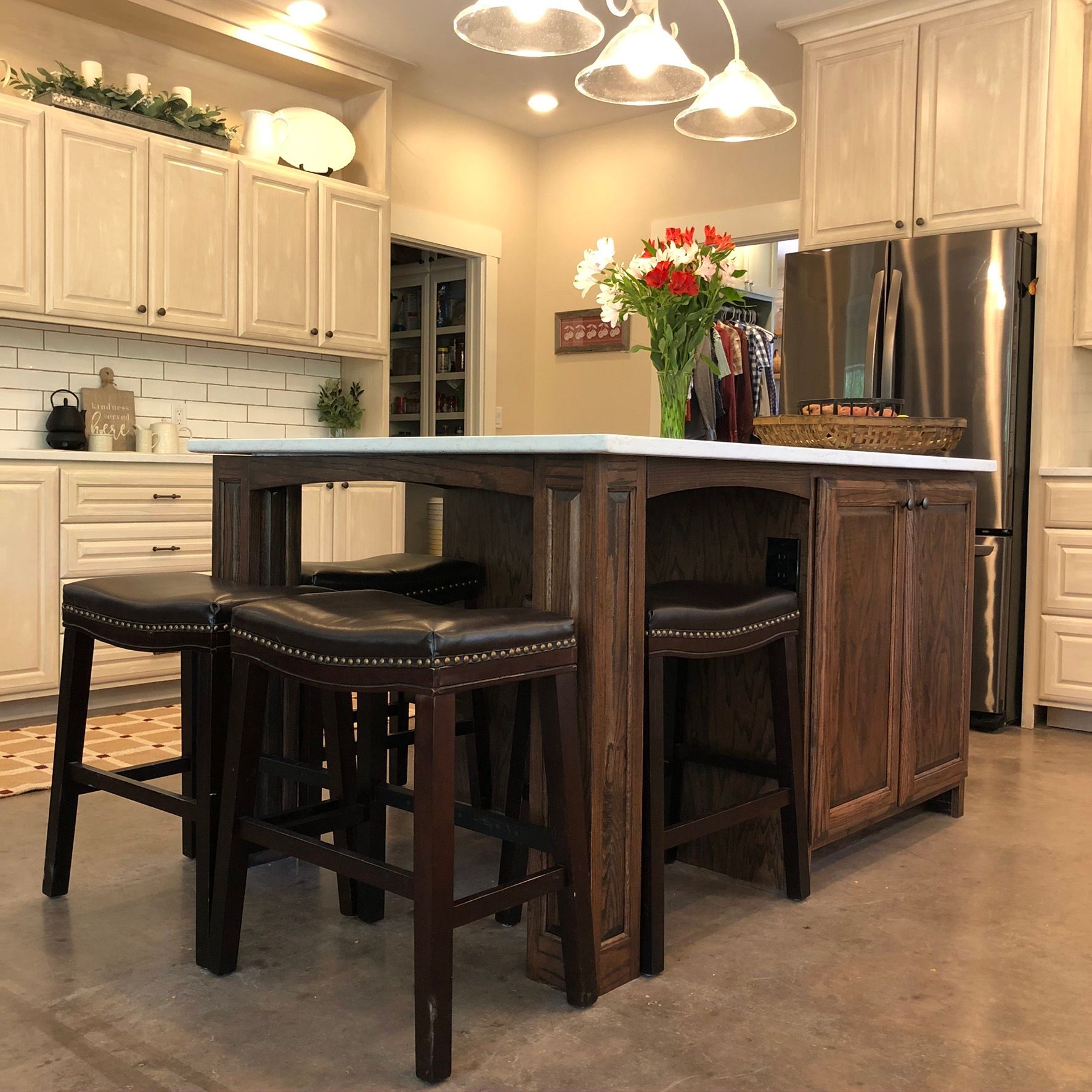Kitchen island with three stools, white countertop, dark wood cabinets, and stainless steel refrigerator.