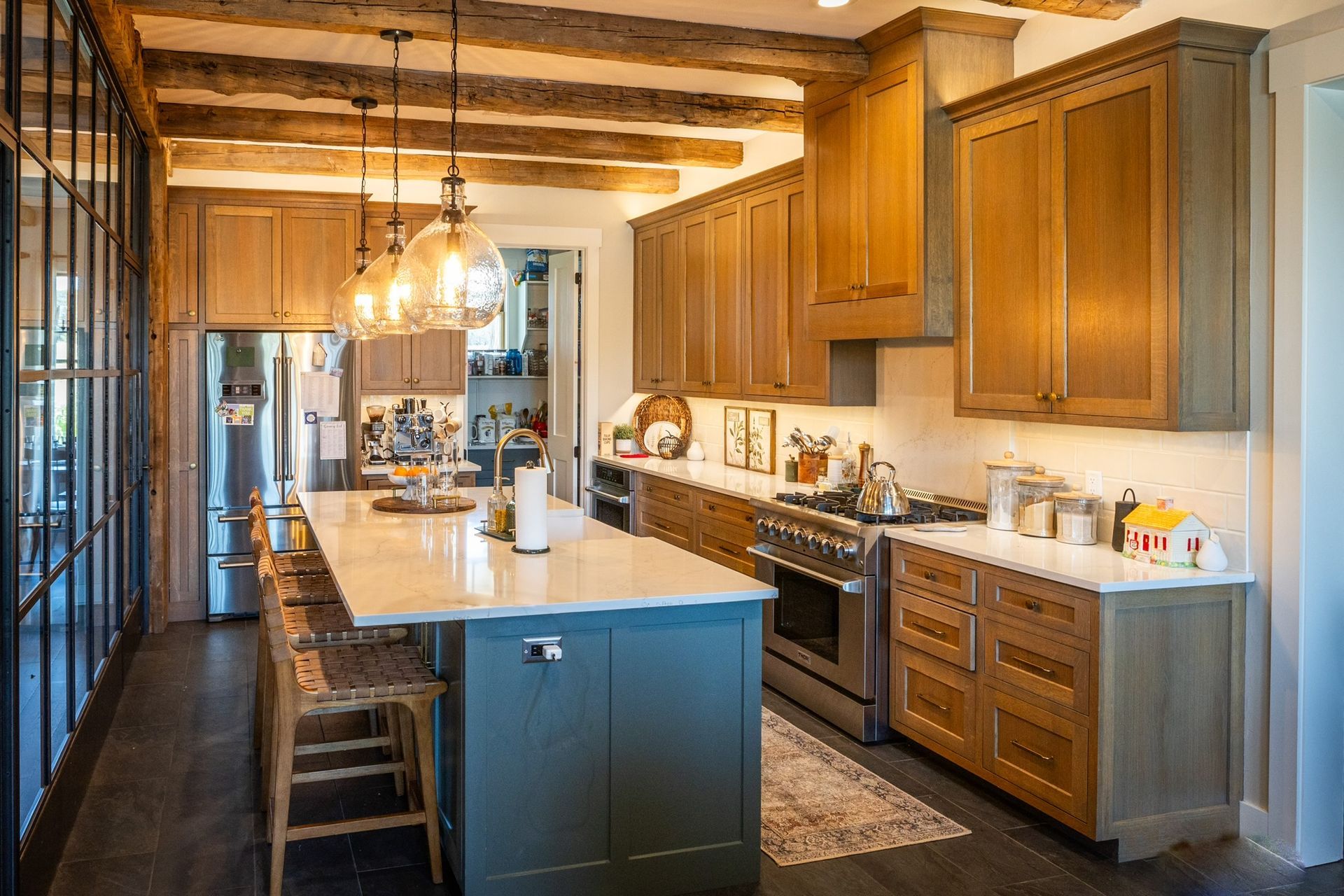 A modern kitchen with wood cabinets, blue island, and large windows.