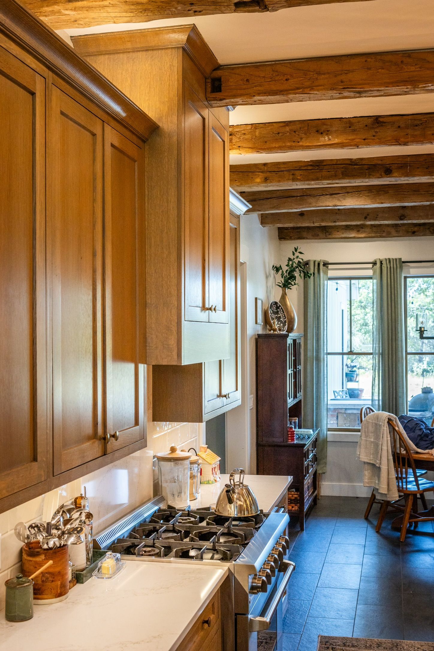 Kitchen with light wood cabinets, gas range, and exposed wooden beams.