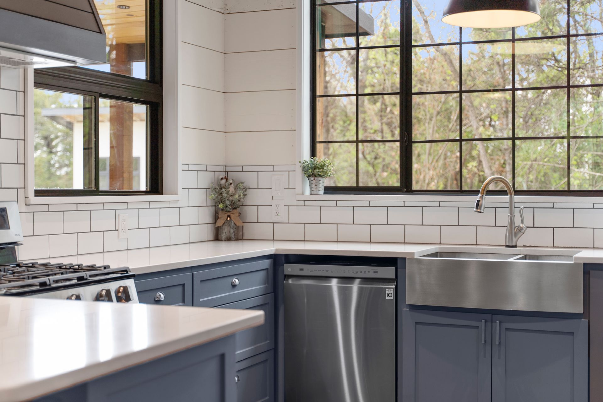 Blue and white kitchen with stainless steel appliances, large windows, and a farmhouse sink.