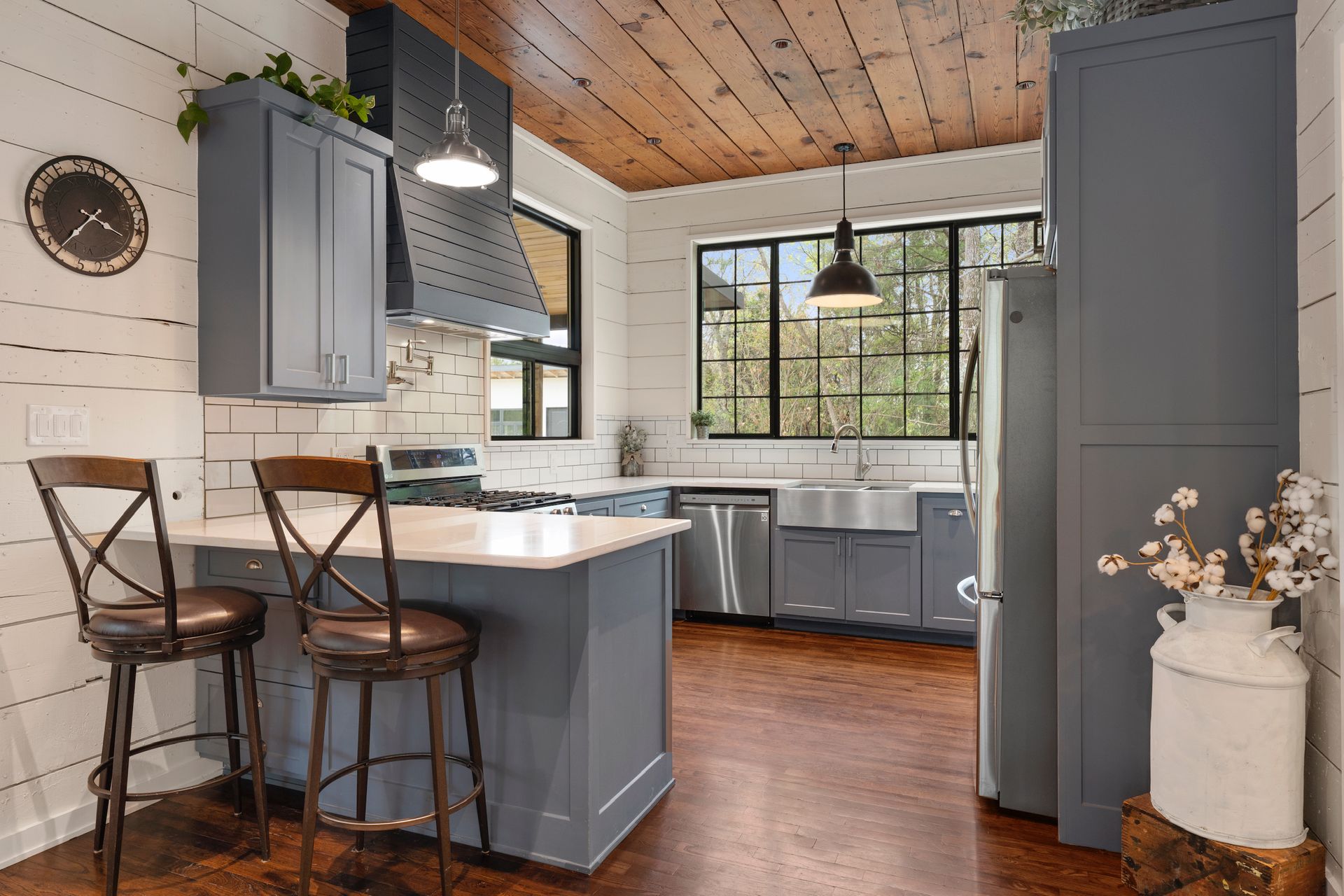 Kitchen with blue cabinets, stainless steel appliances, wood ceiling, and island with bar stools.