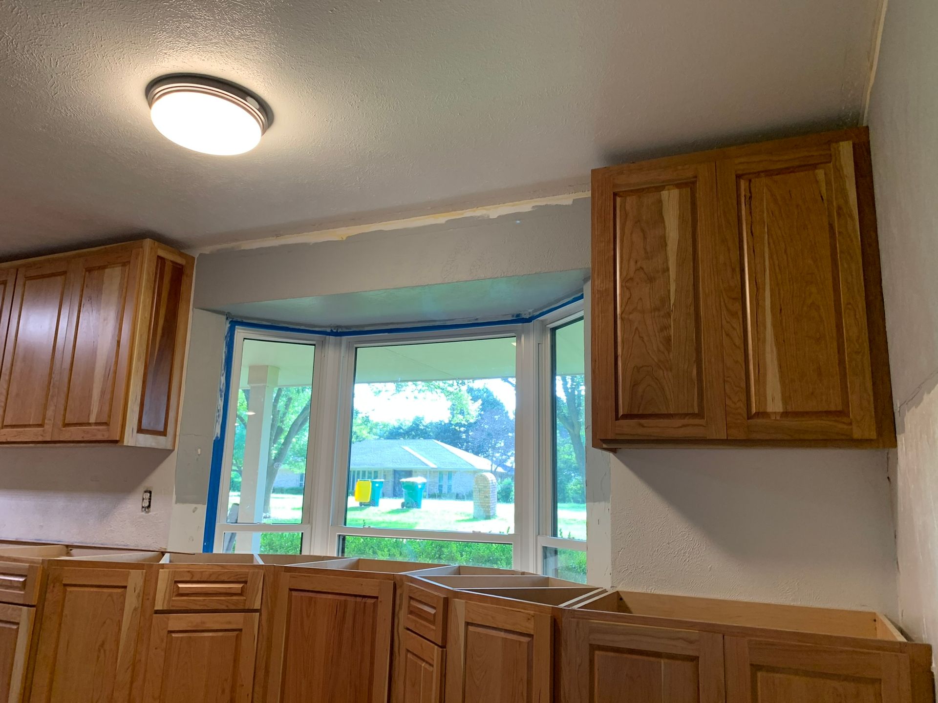 Kitchen with light-colored cabinets, a window, and a ceiling light. Walls are partially painted.
