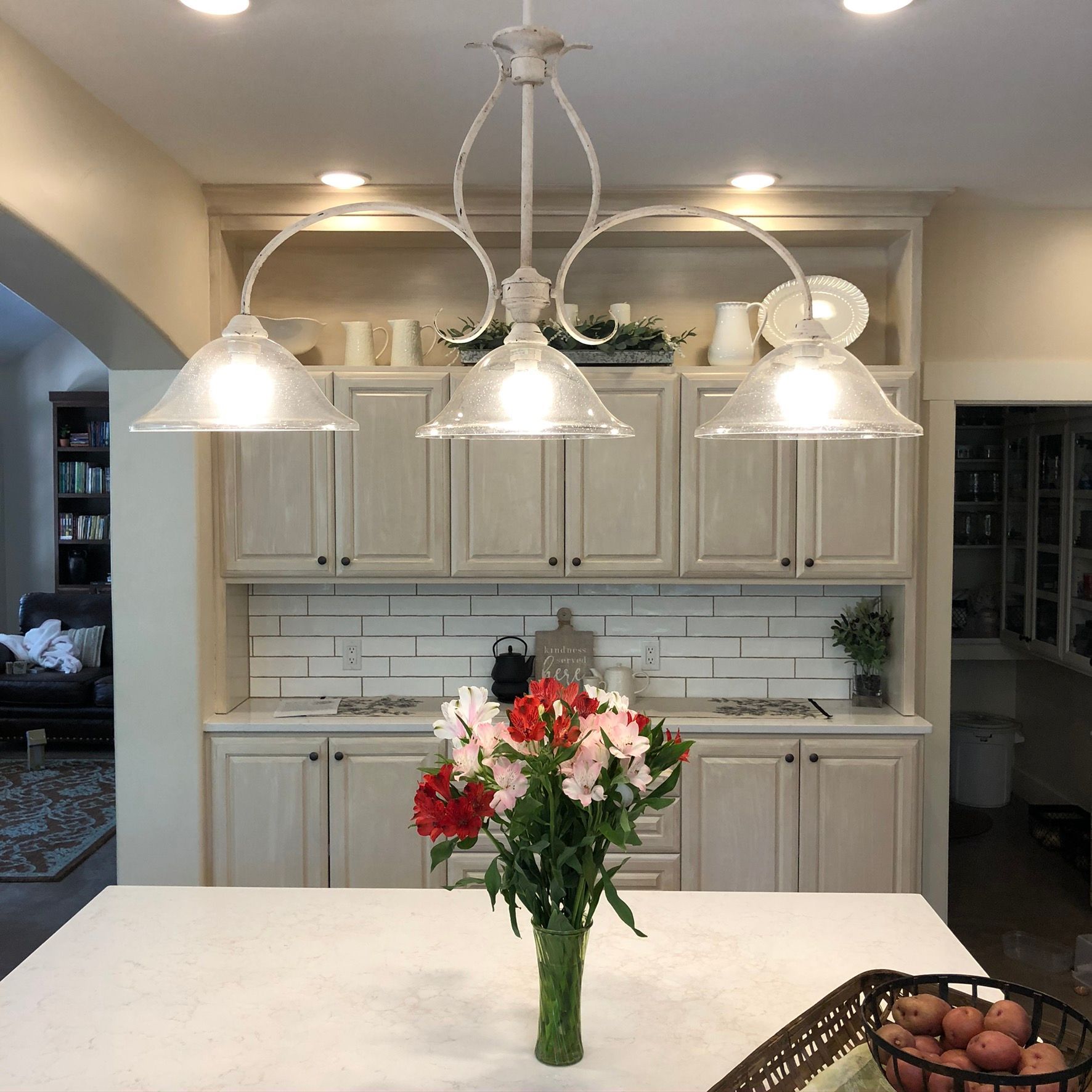 Kitchen with off-white cabinets, a white countertop, and a hanging light fixture. A vase of flowers sits on the countertop.