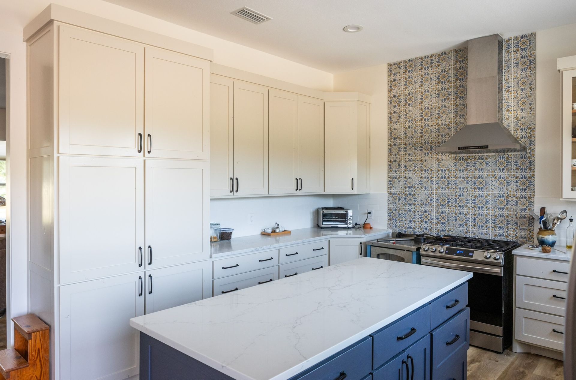 Modern kitchen with white cabinets, blue island, and patterned backsplash.