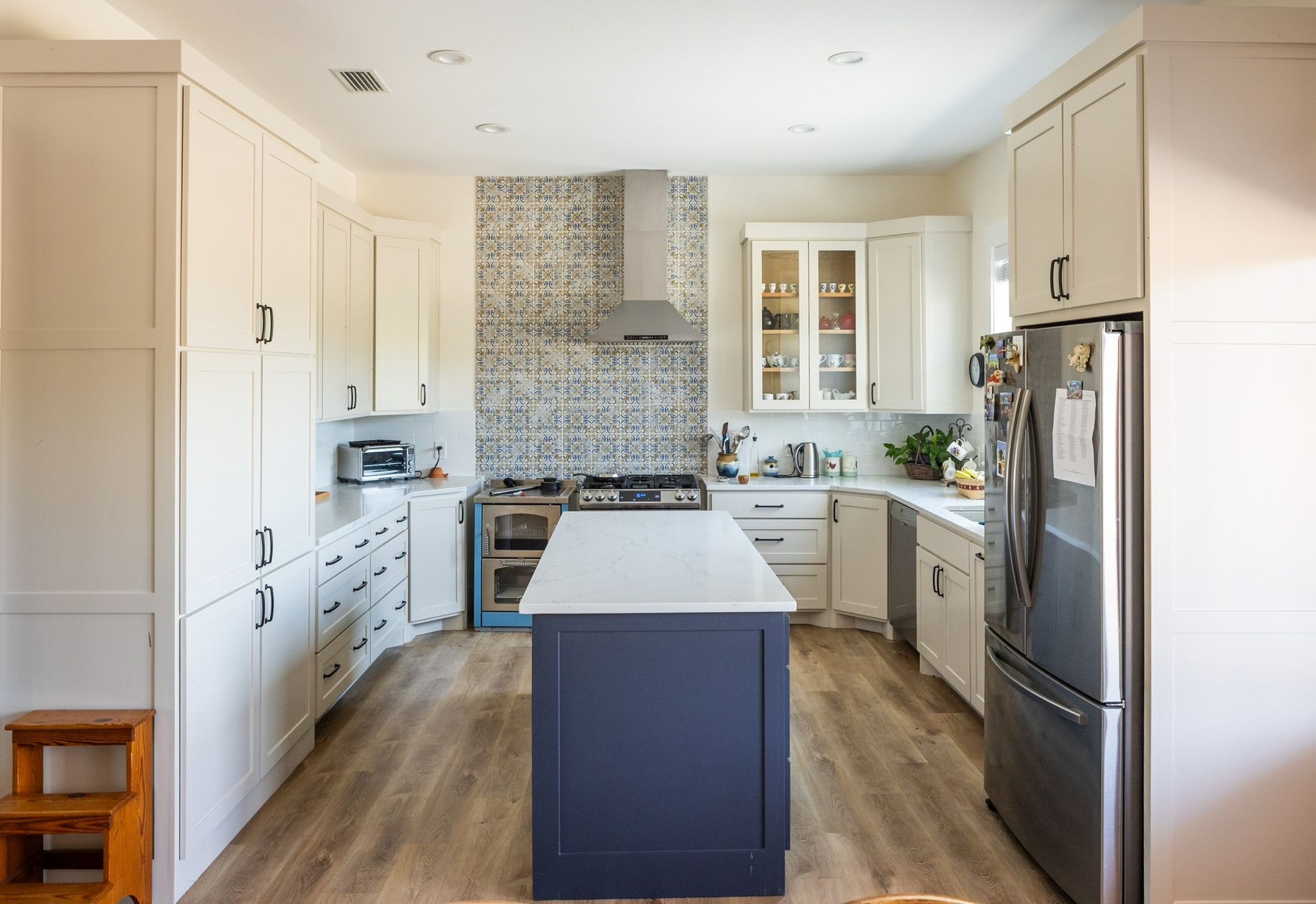 Kitchen with white cabinets, blue island, patterned backsplash, and stainless steel appliances.