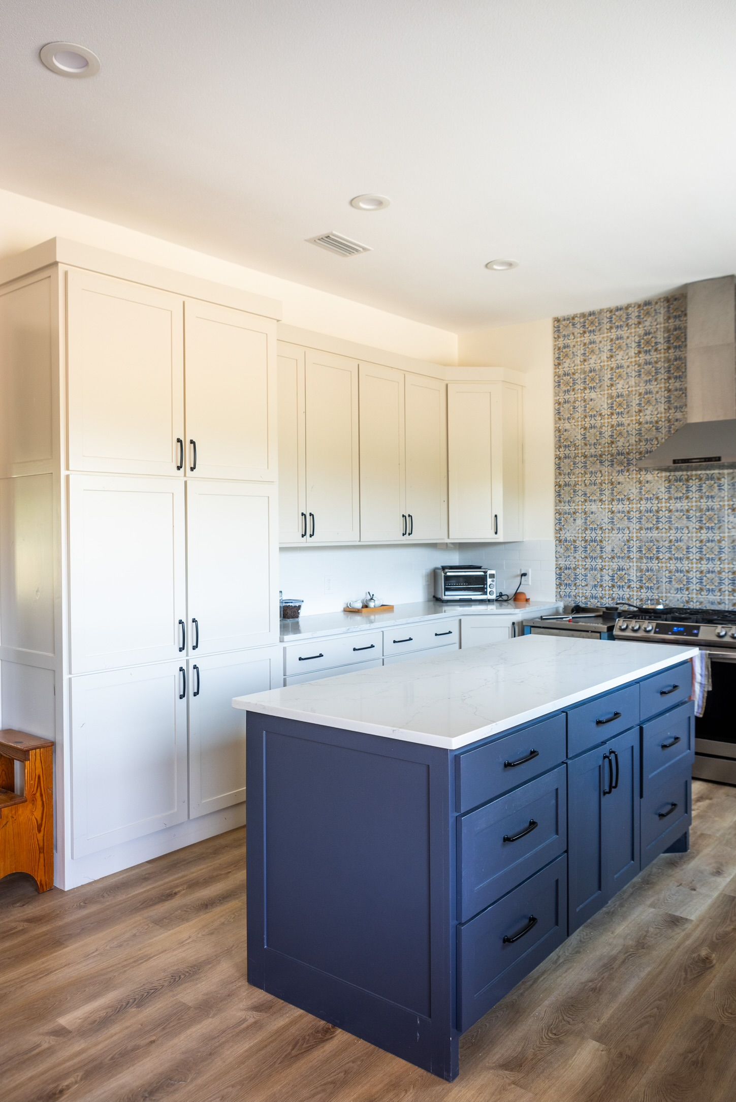 Kitchen with white cabinets, blue island, and patterned backsplash.