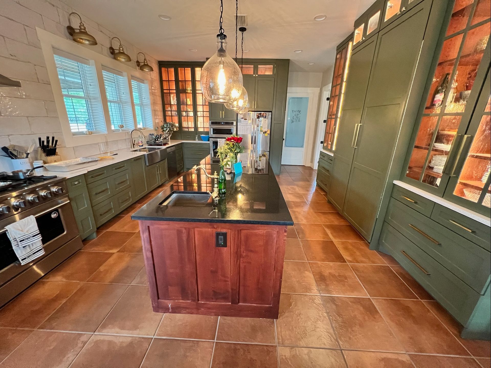 Kitchen with green cabinets, a dark-topped wooden island, and brown tiled floor.