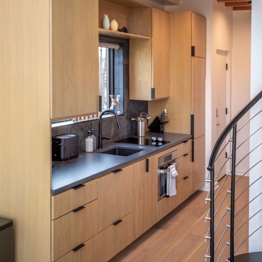 Modern kitchen with light wood cabinets, black countertops, and stainless steel appliances.