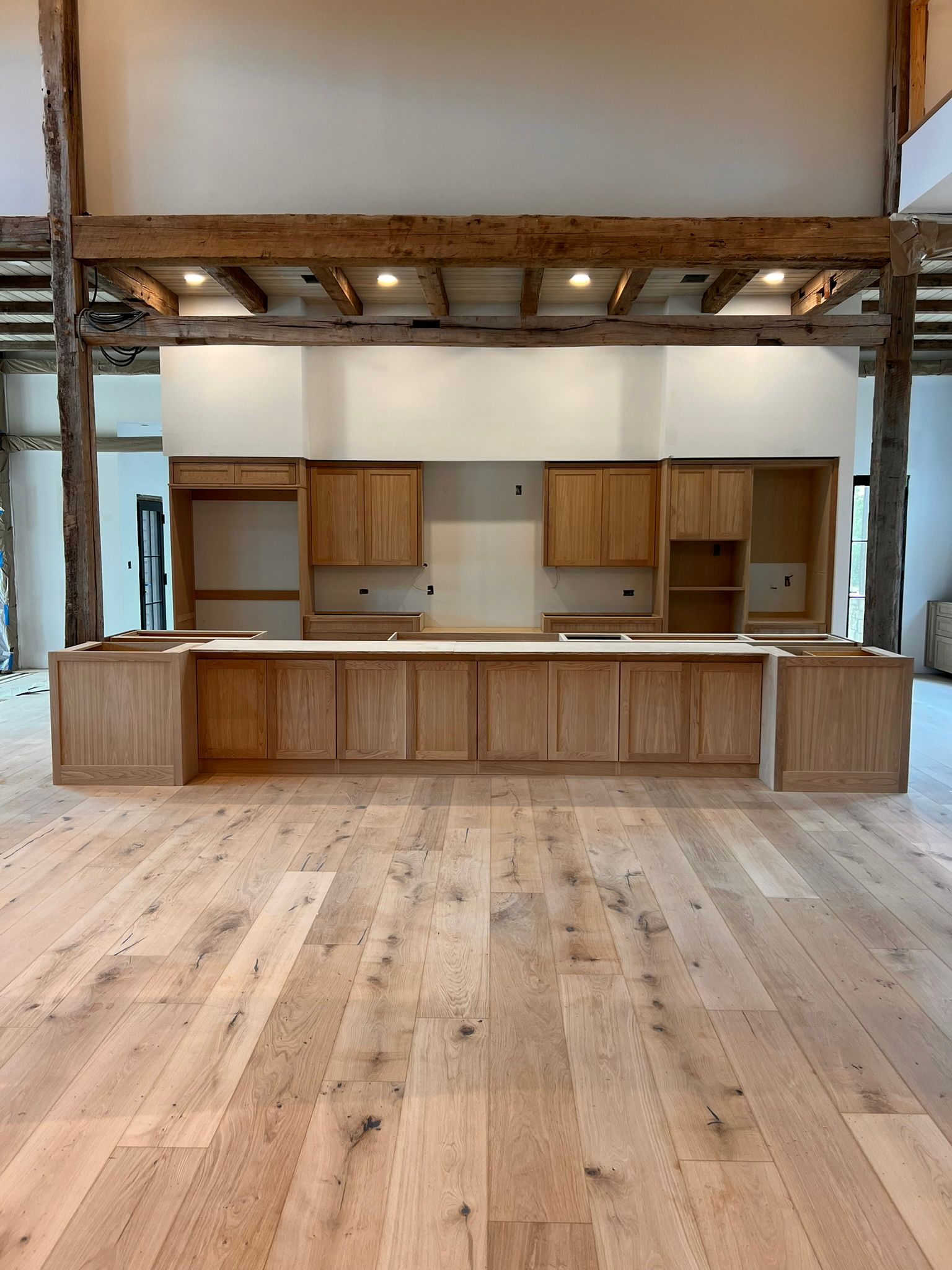 Large kitchen island with light wood cabinets and a beam ceiling.