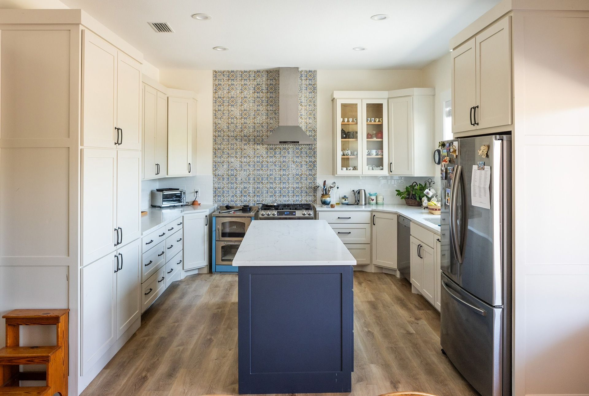 Modern kitchen with white cabinets, blue island, stainless steel appliances, and patterned backsplash.