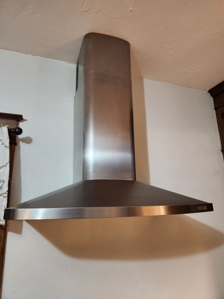 Stainless steel range hood mounted on a white kitchen wall.