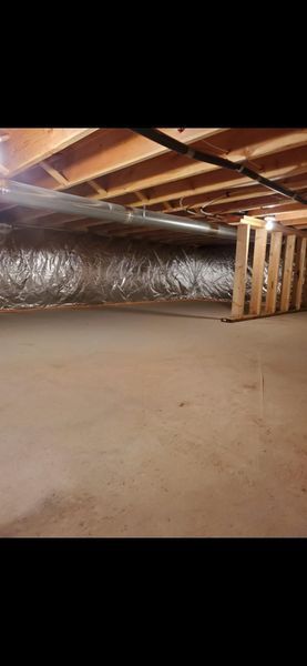 Underneath a house: A crawl space with wooden beams, insulated ductwork, and a wooden pallet.