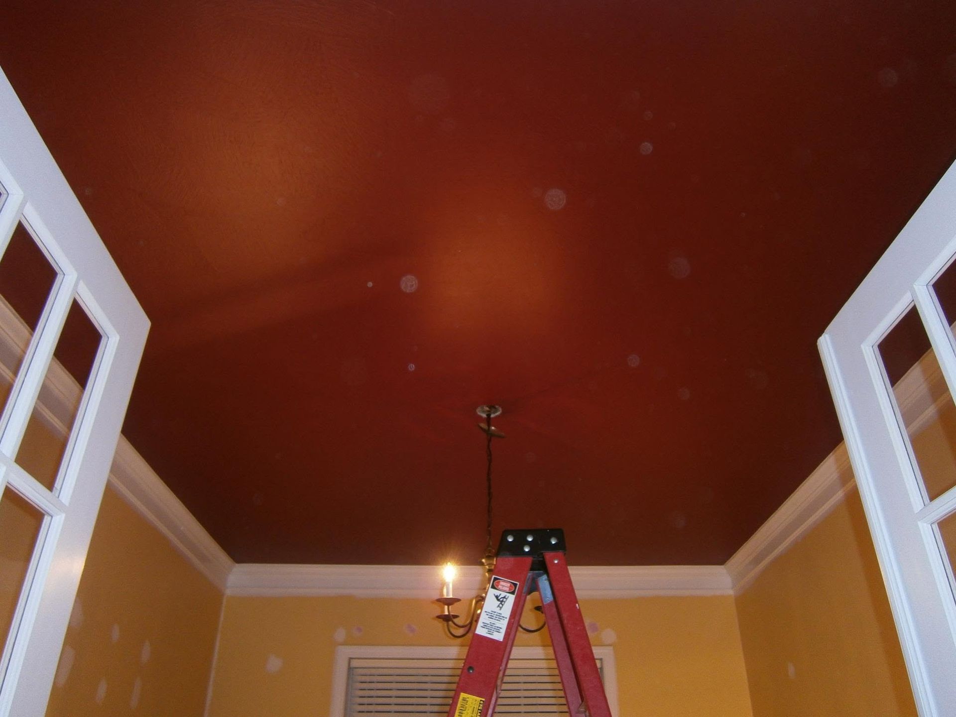 Red ceiling in a room with a red ladder and open white window shutters on both sides.