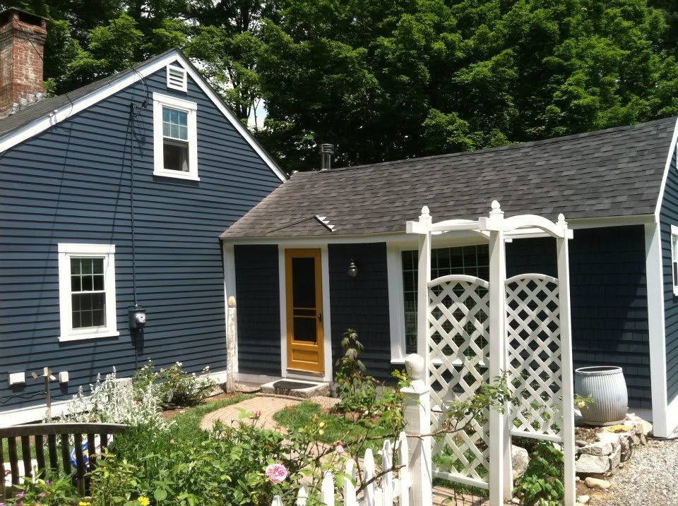 Blue house with white trim, small porch, and white garden arbor in a flowered yard