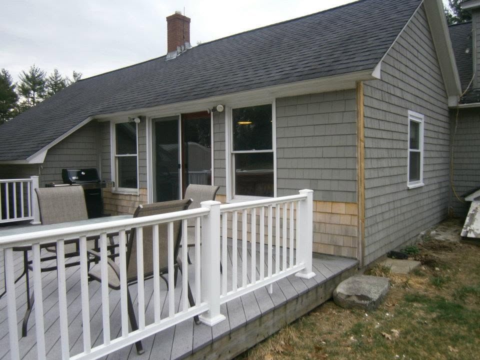 Small gray house with white deck railings and a sloped roof, viewed from the backyard