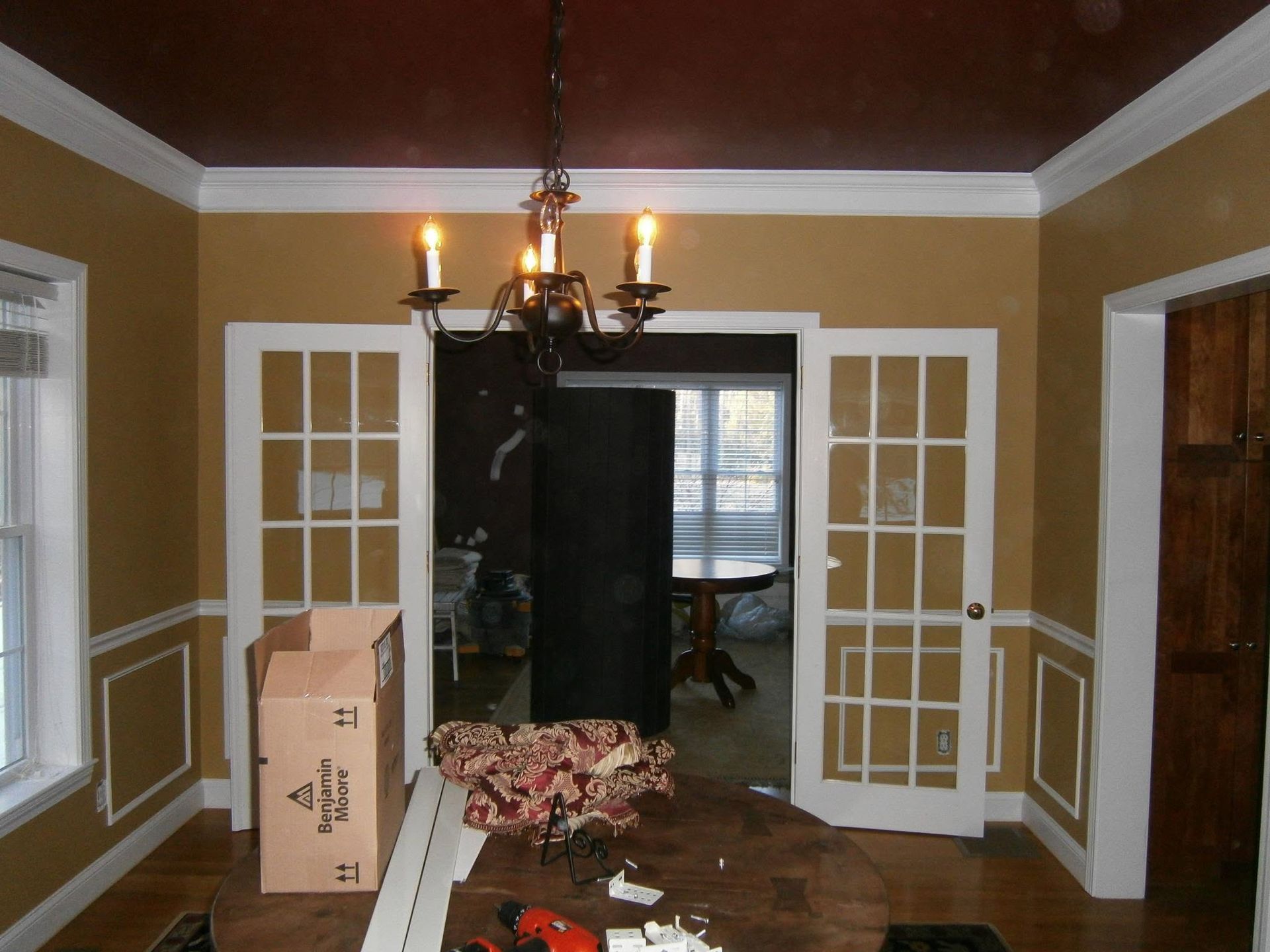 Empty dining room with chandelier, French doors, cardboard box, and a broken chair on the floor
