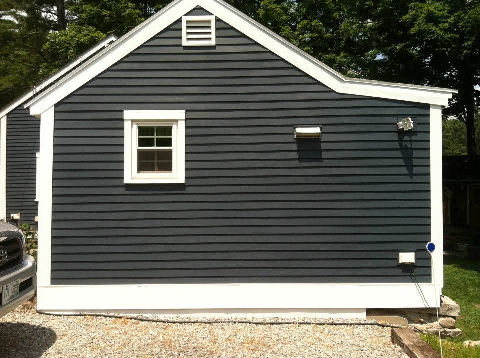 Dark gray house exterior with white trim, a small window, and gravel in front