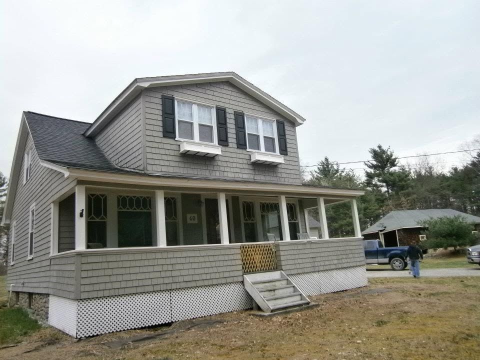 Gray two-story house with a front porch and steps on a dirt lot under a cloudy sky