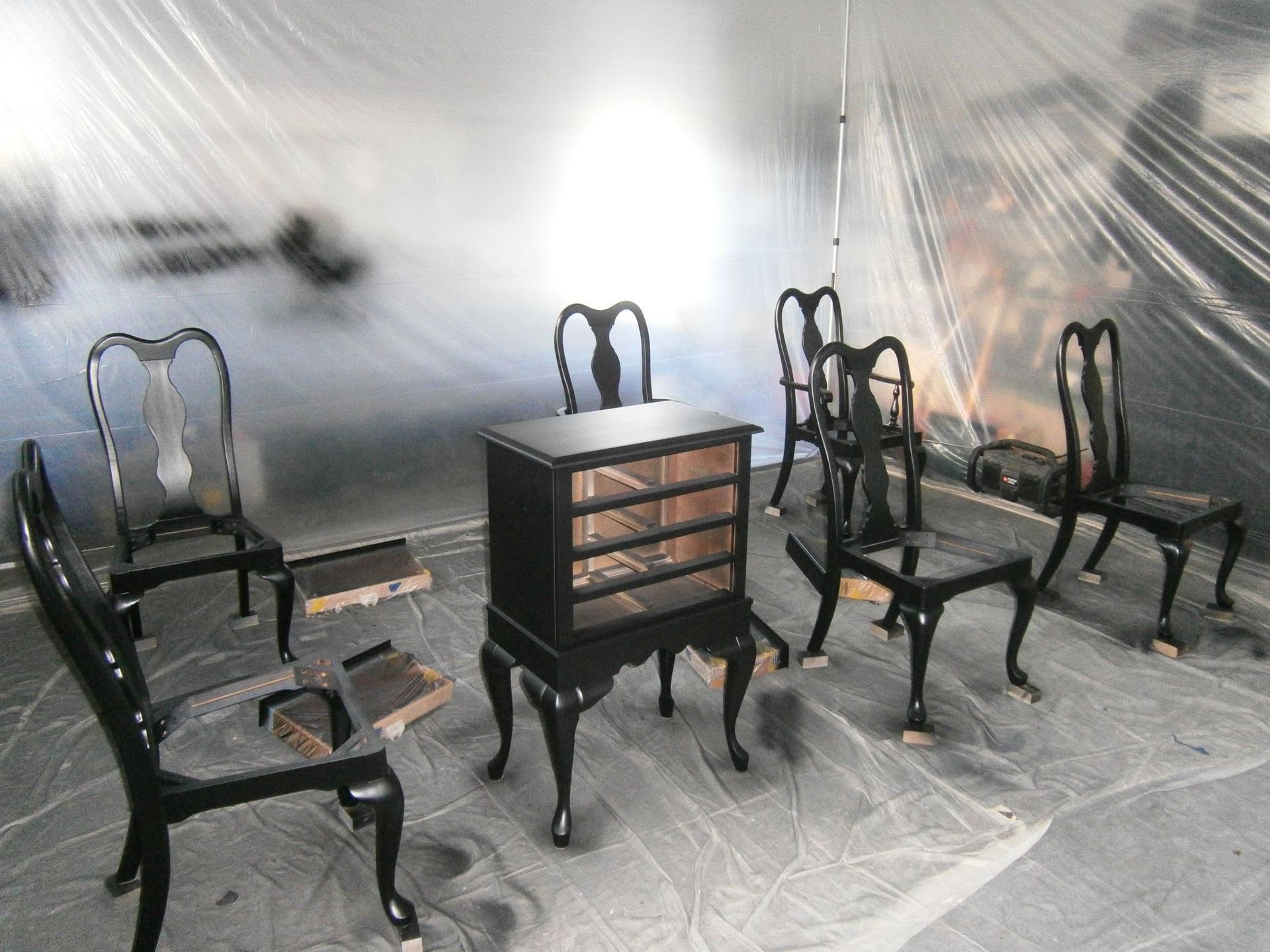 Black wooden chairs and a small drawer cabinet arranged in a bright room with a covered floor.