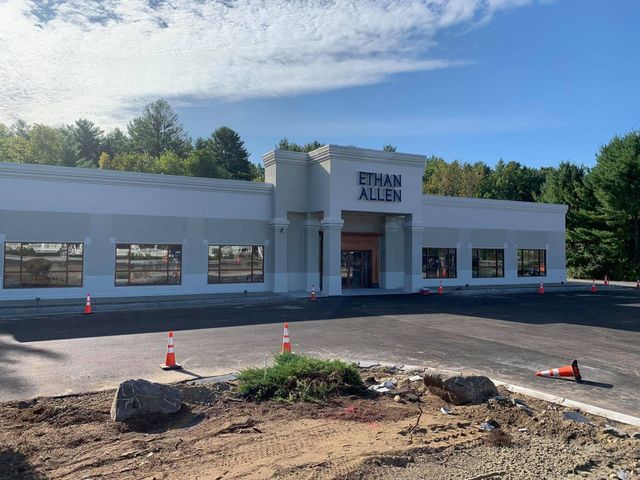 Empty storefront with “ETHAN ALLEN” sign, white facade, and orange cones in a parking lot.