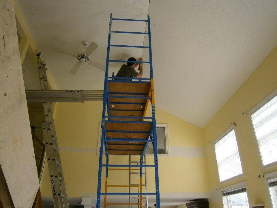 Person on a blue ladder in a yellow room, working near the ceiling.
