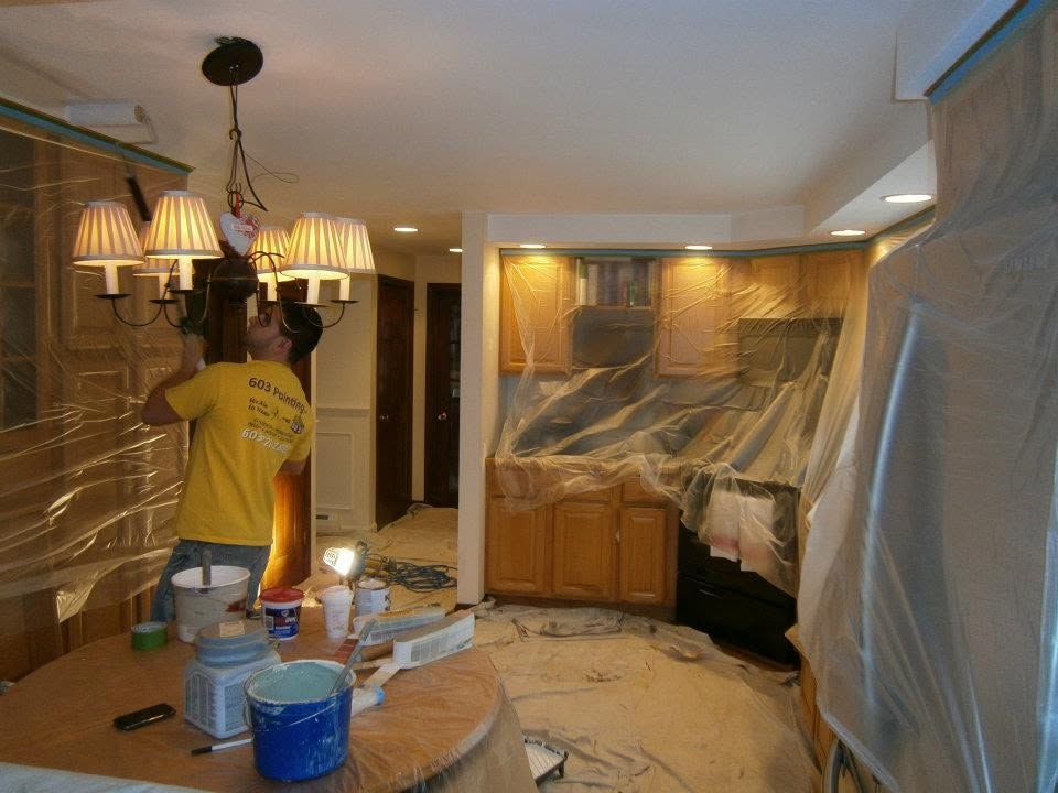 Kitchen under renovation with plastic-covered cabinets and a worker installing a ceiling light.