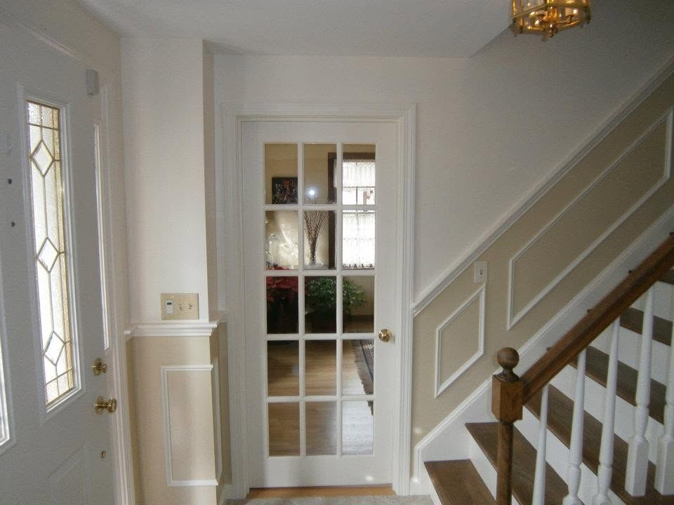 Bright hallway with white walls, a glass-paneled door, and a staircase with wooden railing.