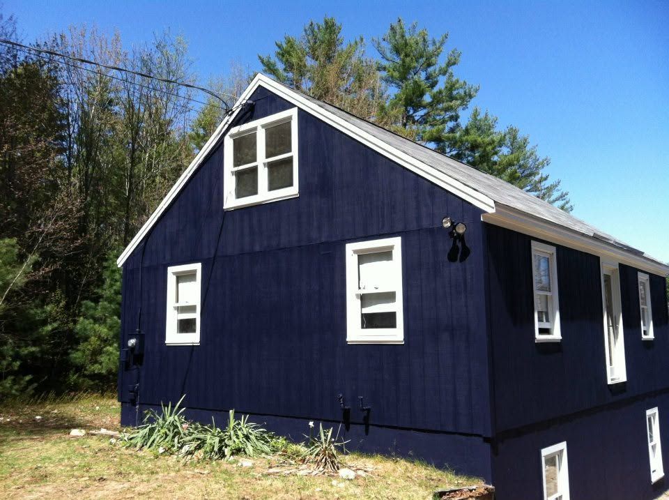 Small dark-blue house with white trim and windows, viewed from the side under a clear sky.