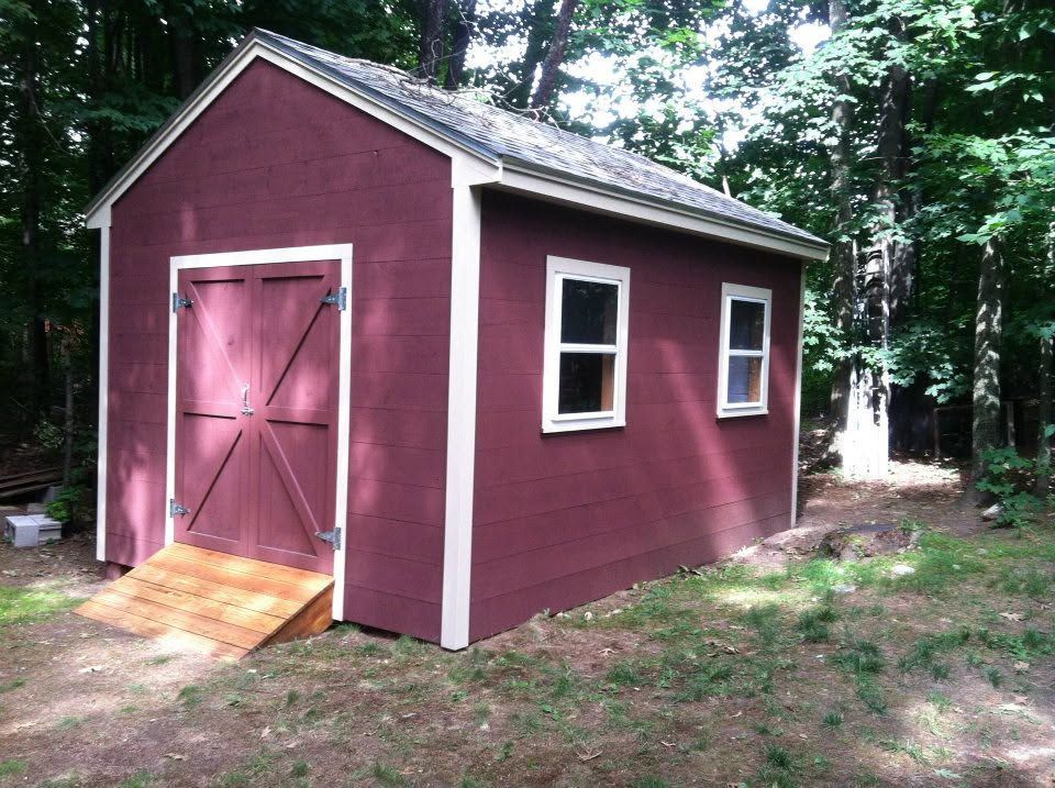 Small maroon shed with white trim and pink double doors in a wooded area