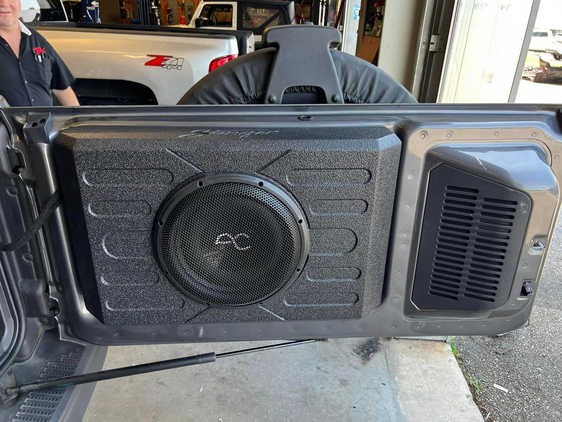A man is standing next to a subwoofer in the back of a truck.