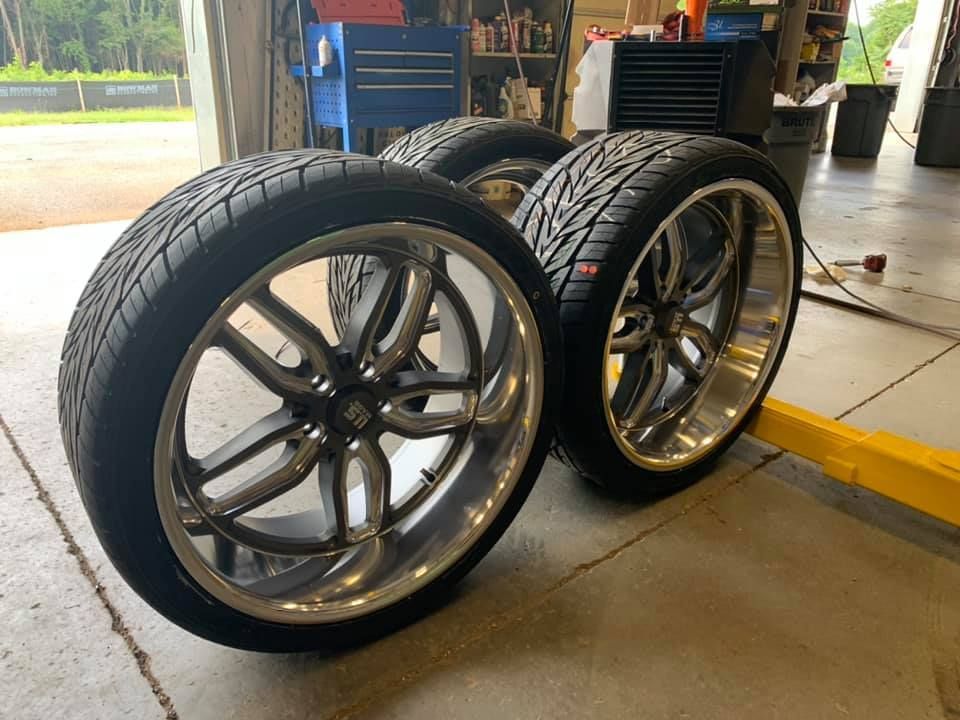 A pair of tires and wheels are sitting on the ground in a garage.