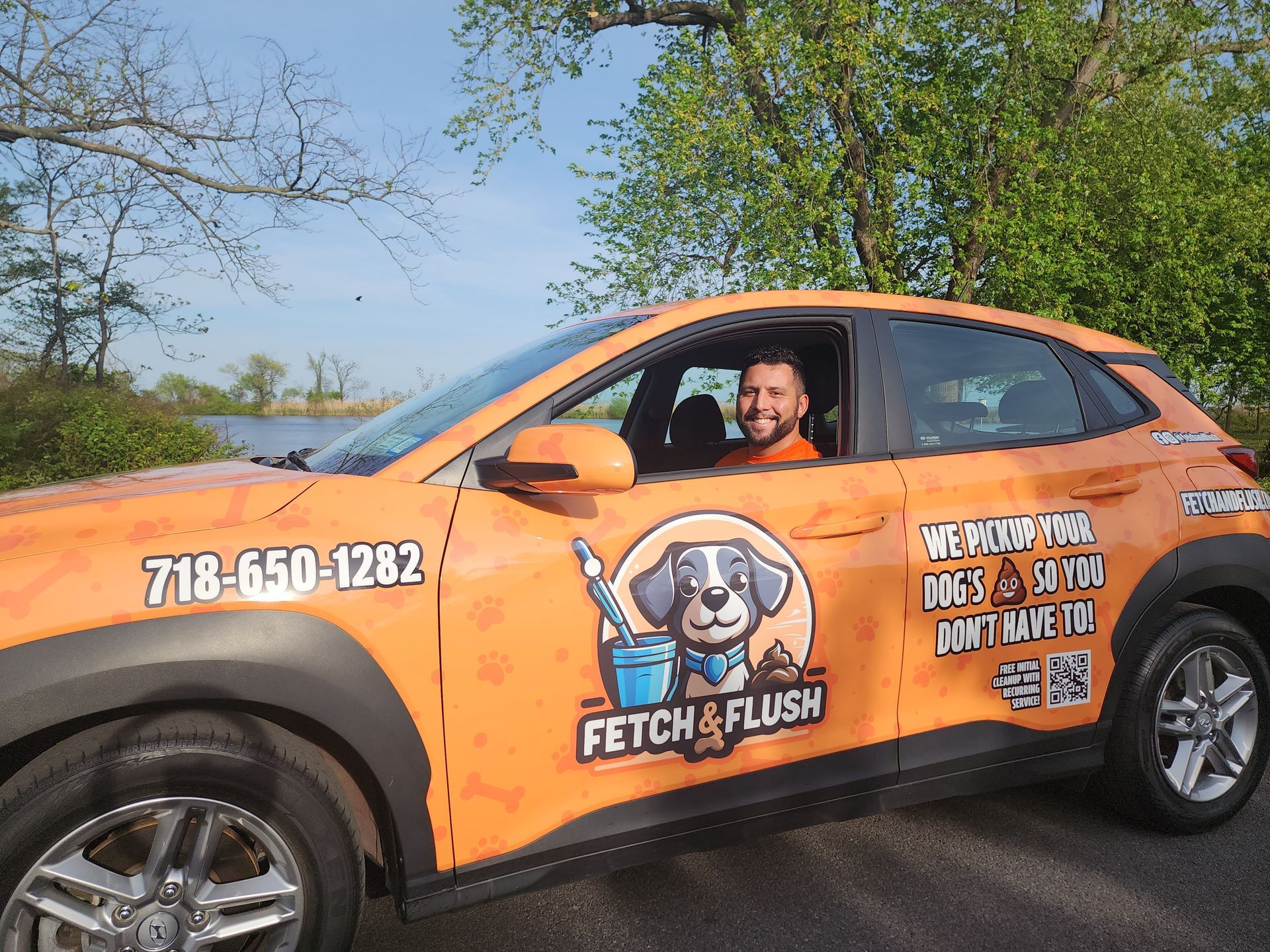 Man in an orange car with "Fetch & Flush" logo. He's smiling. Car has business phone number.