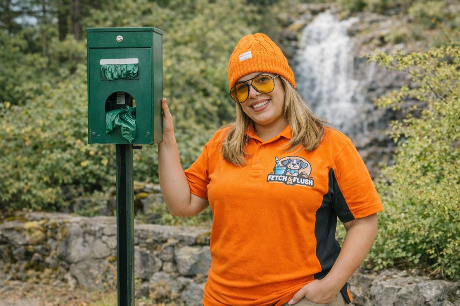 Woman in orange shirt and beanie by a dog waste bag dispenser
