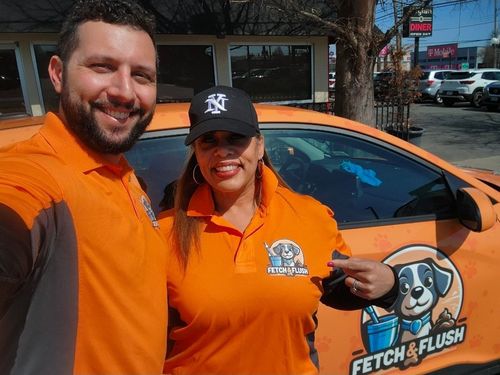 Two people in orange polo shirts posing beside a branded orange vehicle with a dog logo.